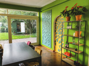 Groene vergaderruimte met houten tafel, kleurrijke stoelen en planten in een kantooromgeving.