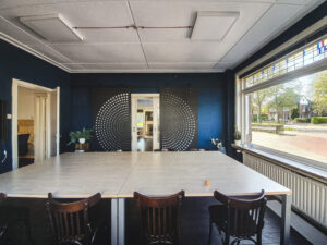 Vergaderruimte met lange witte tafel, donkerblauwe wand en rond raam