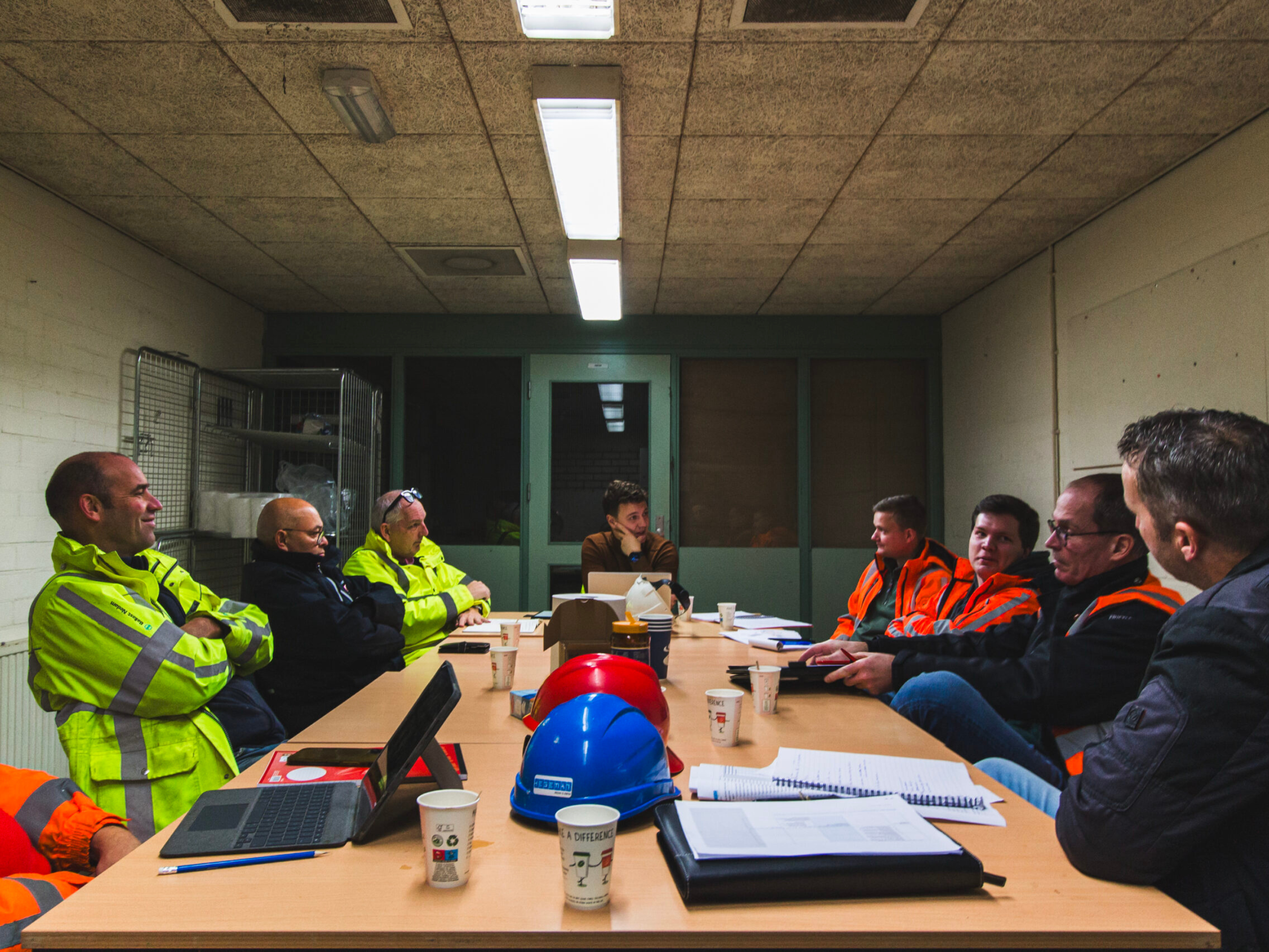 Bouwoverleg met mensen in veiligheidshesjes rond een tafel