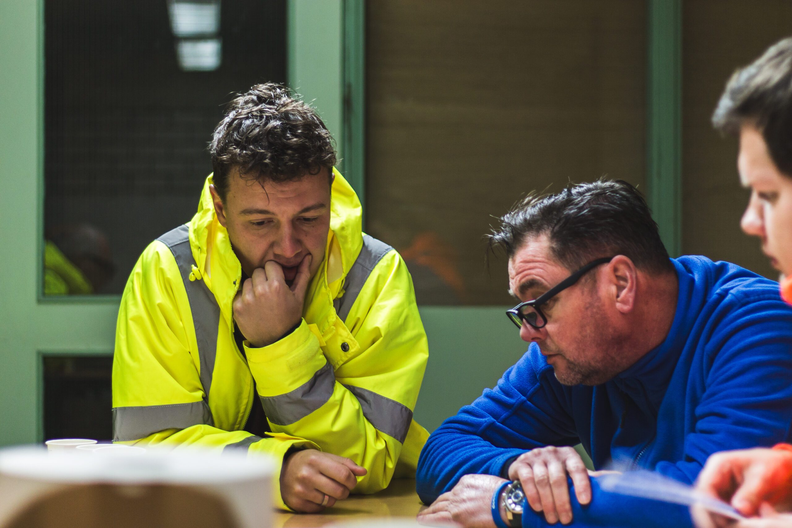 Twee collega's in veiligheidshesjes bespreken plannen aan tafel